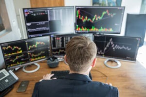 A broker at his computer in front of several monitors engaged in excessive trading.