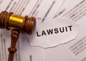 Wooden gavel next to a piece of paper with the word “Lawsuit” written on it, with someone nearby wondering if they can file a lawsuit against OKX